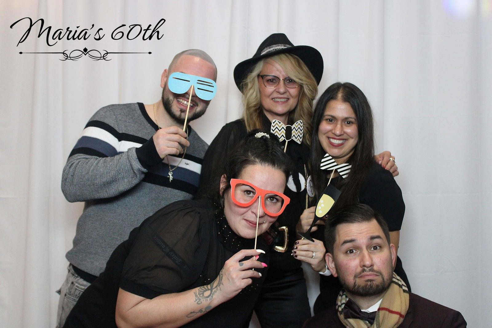 Five friends posing playfully with props and smiles at a 60th birthday party.