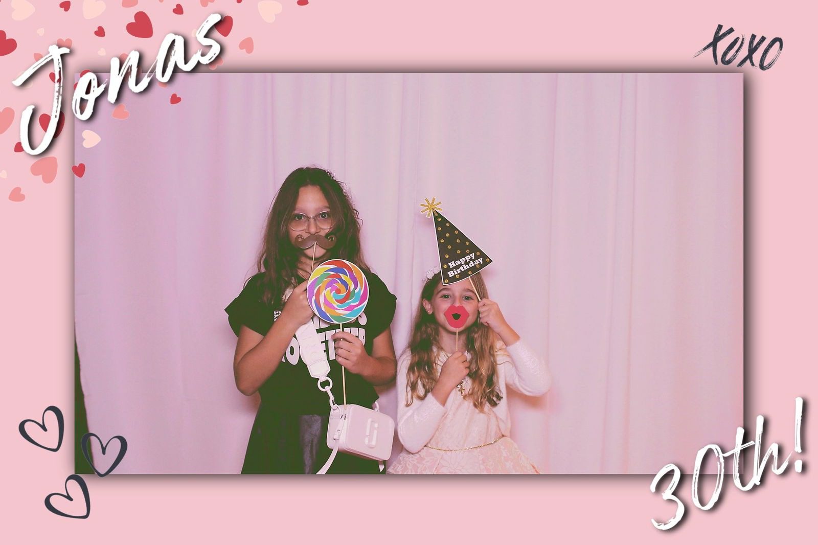 Two girls posing with party props against a pink backdrop.