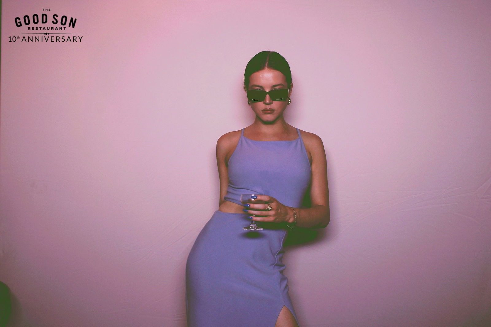 Woman in a stylish purple dress holding a glass, wearing sunglasses.