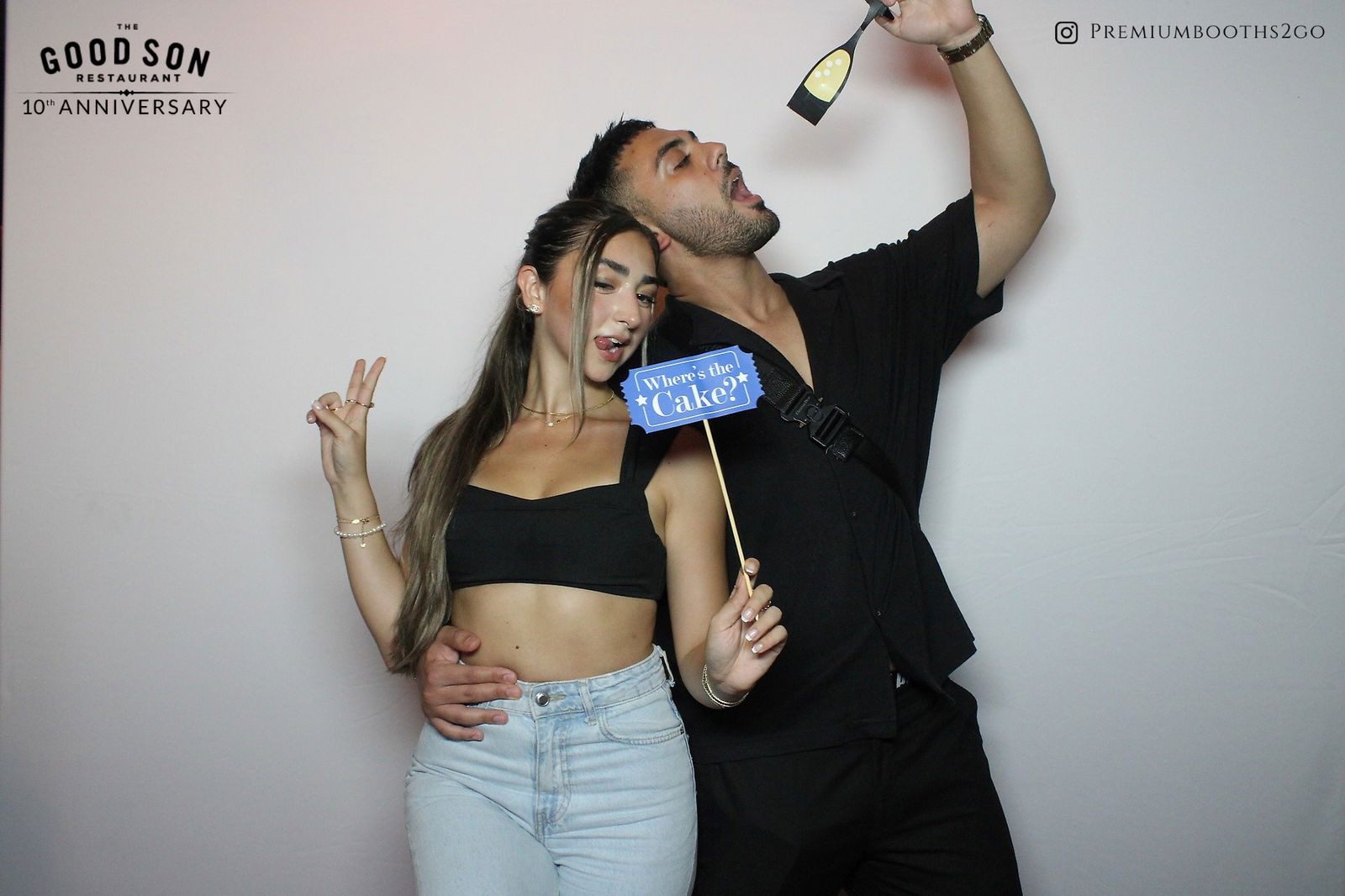 A couple posing playfully with photo booth props against a white backdrop.