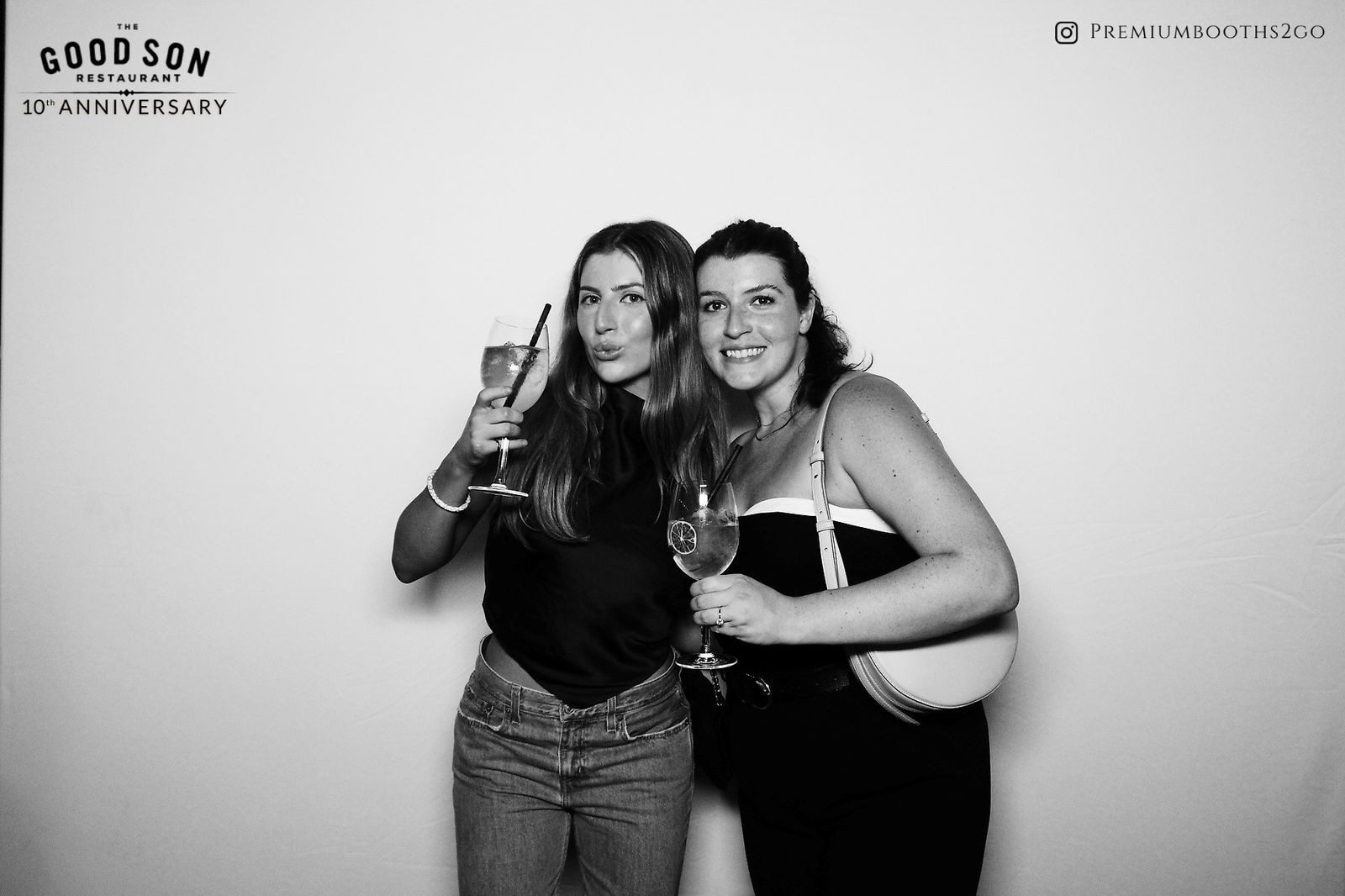 Two women smiling and posing with drinks in a black and white photo.