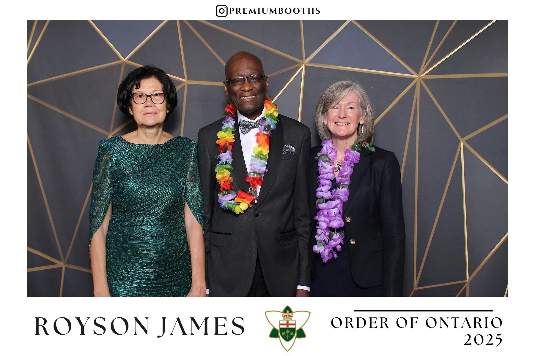 Three people smiling, dressed formally with leis, standing in front of a geometric backdrop.